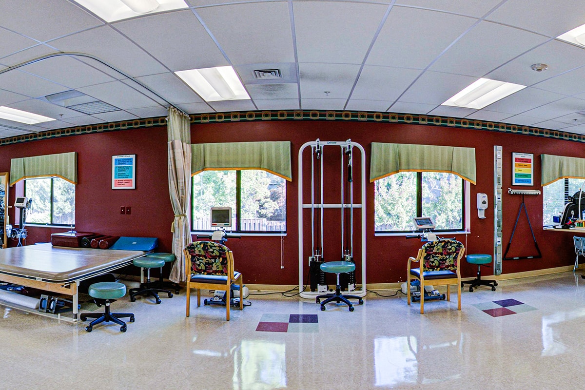 Rehab gym with four large windows and other physical therapy equipment.