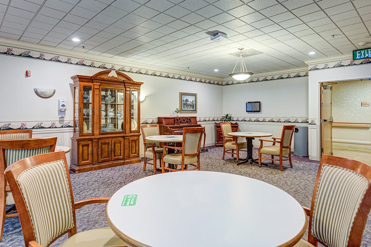 Dining/activity room with round tables and chairs, china cabinet, carpet and chandeliers