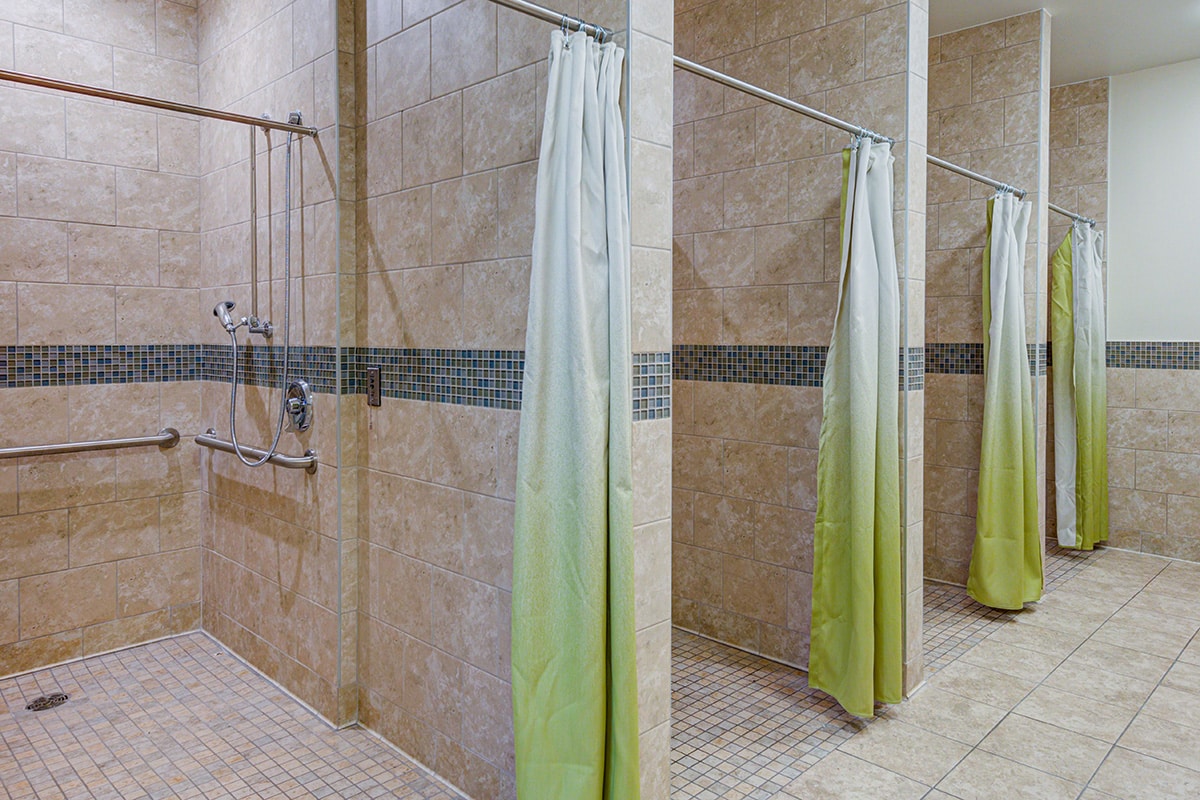 Bathroom with four large tiled walk-in showers with green shower curtains