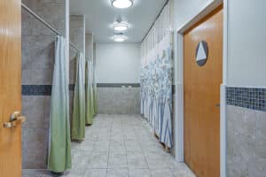 Bathroom with four large tiled walk-in showers with green shower curtains from hallway angle
