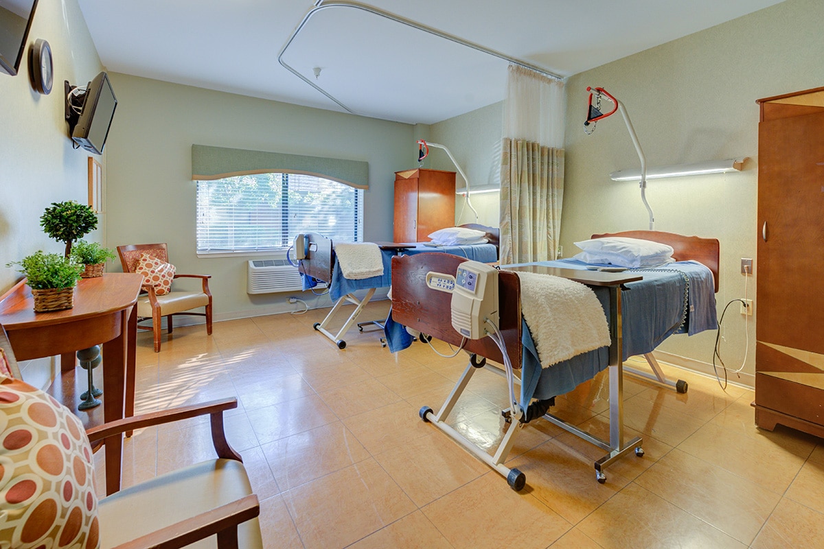 Double occupancy room facing flat screen tv and large window, with beds with blue bedding