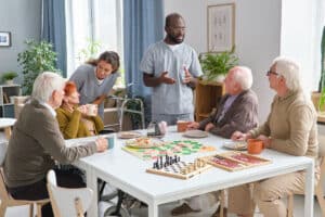 residents sitting at table with skilled nursing staff eating pizza and playing games like chess